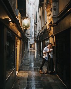 a man and woman kissing in an alleyway next to each other with buildings on either side