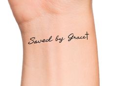 the word saved by grace written in black ink on a woman's wrist