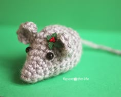 a crocheted mouse with holly leaves on it's head sitting on a green surface