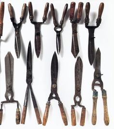 an assortment of old knives and pliers hanging on a white wall with clippings