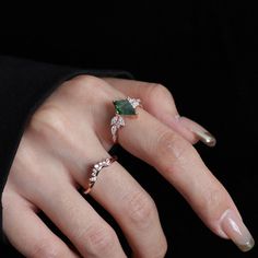 a woman's hand with two rings on it and an emerald stone in the middle