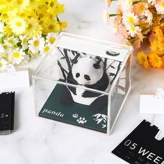 a glass box with a panda sticker on it next to some flowers and tags