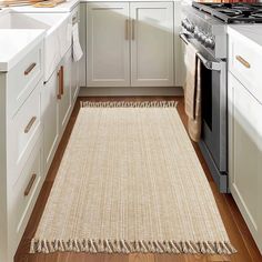 a kitchen with white cabinets and wood flooring has a beige rug on the floor