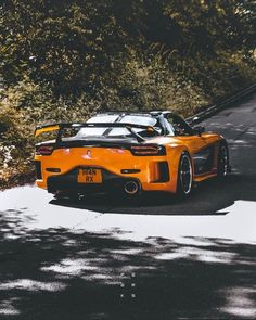 an orange sports car driving down a road next to some bushes and trees in the background