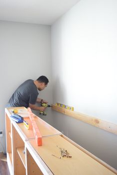 a man is working on the wall in his room with some screwdrivers and tools