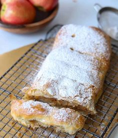 two pieces of bread sitting on top of a cooling rack with apples in the background