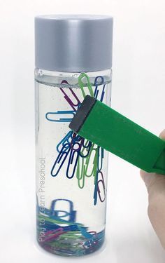 a hand holding a green plastic clip next to a water bottle filled with paper clips