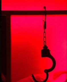 a swing hanging from a chain in front of a red wall with a pink light behind it