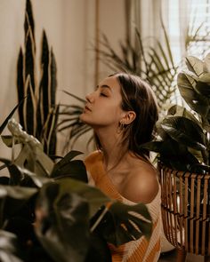 a woman is sitting in front of some plants and looking up at the sky with her eyes closed