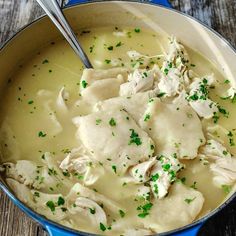 a blue pot filled with chicken and dumplings on top of a wooden table next to a spoon