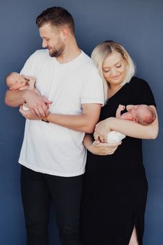 a man and woman are holding their newborn baby while standing against a blue wall with her arms around him