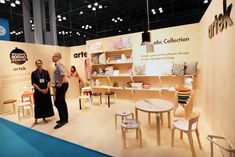 two people standing next to each other in front of a booth with furniture on display