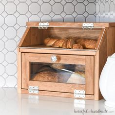 a wooden box filled with bread on top of a counter next to a white vase