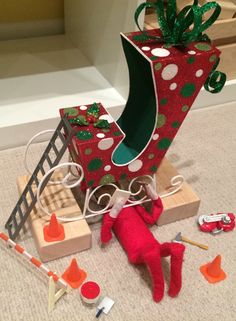 an elf is laying on the floor next to a christmas present box and other toys