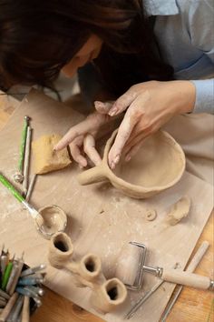 a woman is working with clay on a wooden table next to scissors and other crafting supplies