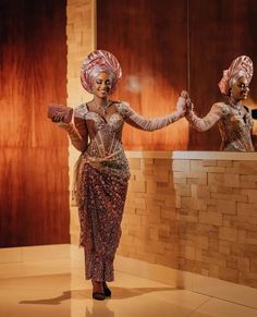 a woman in a dress and turban standing next to a counter with two mirrors behind her