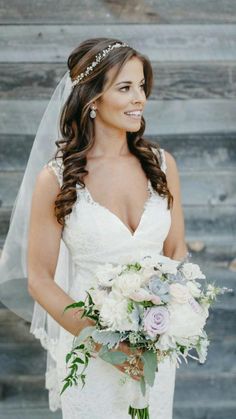 a bride holding her bouquet in front of a rustic wooden wall and wearing a veil