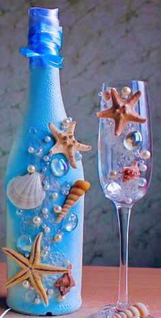 two wine glasses sitting next to a bottle with seashells and starfish on it