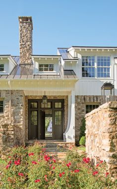 the front entrance to a large home with stone pillars and windows on each side, surrounded by red flowers