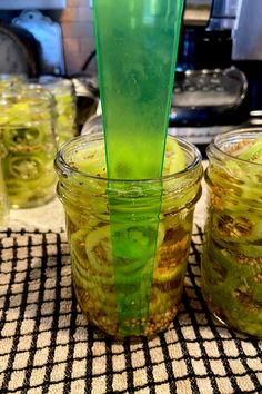 there is a green liquid in the jar and some pickles on the table next to it