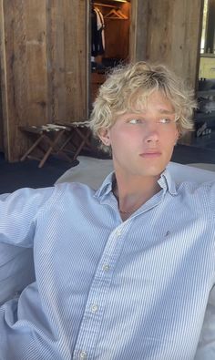 a young man with blonde hair sitting on a couch in front of a wooden wall