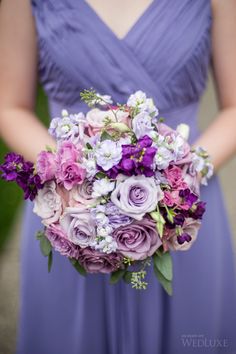 a bridesmaid holding a bouquet of purple and white flowers in her hands,