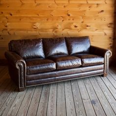 a brown leather couch sitting on top of a wooden floor next to a wall covered in wood planks