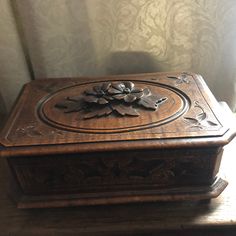 an ornate wooden box sitting on top of a table next to a window with curtains behind it