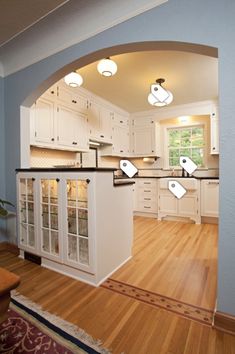 an archway in the middle of a kitchen with white cabinets and wood flooring, along with hardwood floors