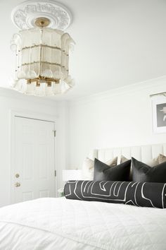 a white bed with black pillows and a chandelier hanging from it's ceiling