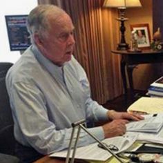 an older man sitting at a desk with papers