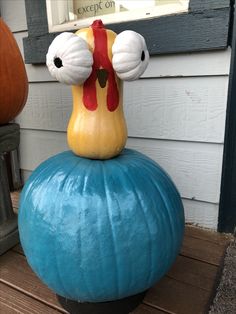 a large blue pumpkin sitting on top of a wooden bench next to a building with a rooster head sticking out of it