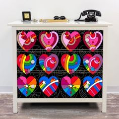 a white cabinet with colorful hearts painted on the front and sides, next to a phone