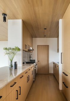 a long narrow kitchen with wooden cabinets and white marble counter tops, along with a vase filled with flowers