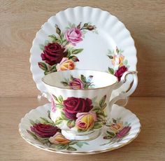 a tea cup and saucer with roses on it sitting on a wooden table top