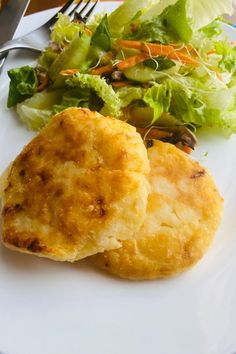 a white plate topped with two scones next to a green leafy salad and fork