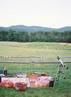 an open field with blankets and bags on the ground near a camera set up in front of a wooden fence