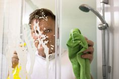 a man wiping his face with a green towel in front of a shower door while holding a yellow rag