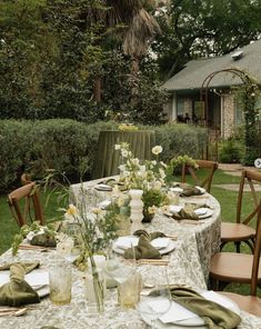 an outdoor table set with plates and napkins for dinner in the garden, surrounded by greenery