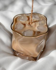 an iced drink being poured into a glass with ice cubes in it on a white blanket