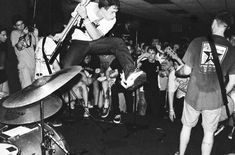 a man is jumping in the air with his guitar while people watch from behind him