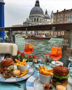 two plates with sandwiches and french fries are sitting on a table overlooking the water in venice