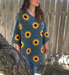 a woman standing next to a tree wearing a blue crocheted sweater with sunflowers on it