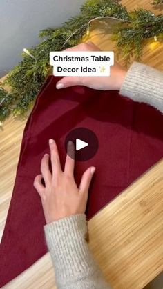 a person is making a christmas table decoration idea with red fabric and green garlands