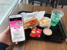 a person holding up a cell phone next to a tray with food and drinks on it