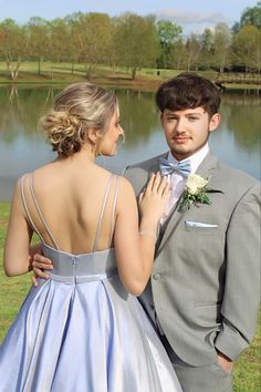 a young man and woman standing next to each other in front of a body of water