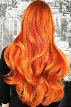 a woman with bright orange hair in front of a cityscape background and the back of her head