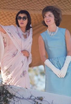 two women in blue dresses and white gloves standing next to each other with their arms outstretched