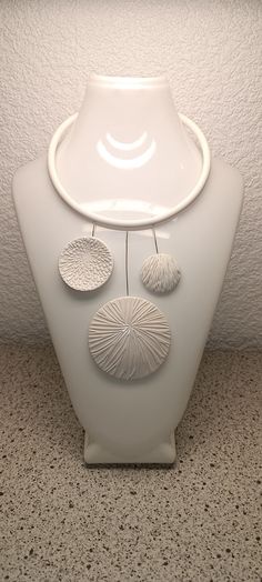 a white vase sitting on top of a floor next to a wall with three circles