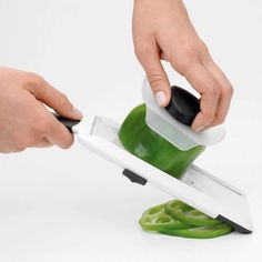 a person using a knife to cut green peppers on a cutting board with a slicer